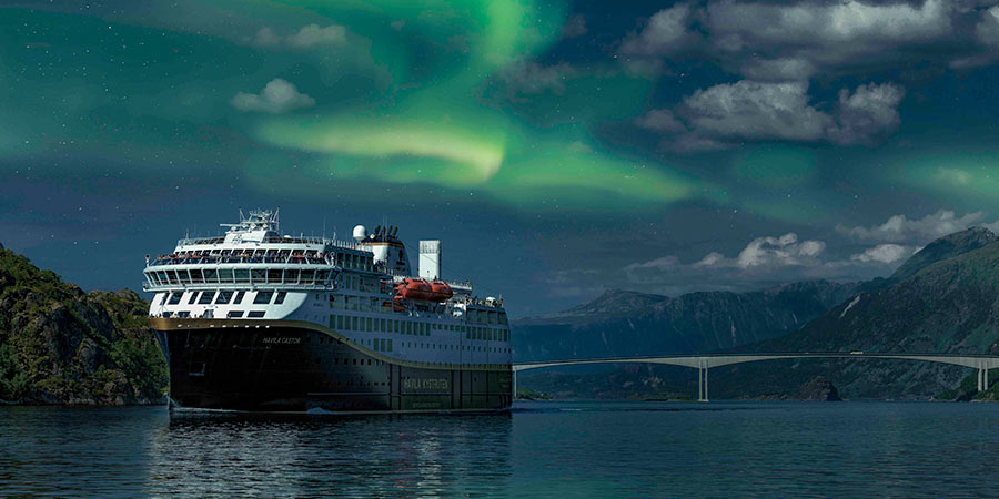 The Northern Lights appear above a Havila cruise ship on a dark night. 